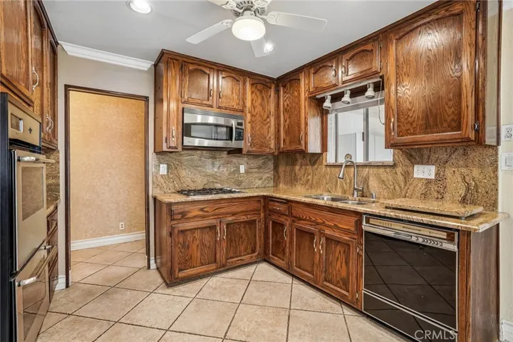 Kitchen - This well-appointed kitchen combines timeless character with functional design, featuring rich wood cabinetry, granite countertops, and a full granite backsplash that adds warmth and elegance throughout the space. Stainless steel appliances, including a built-in oven and microwave, complement the classic finishes, while ample cabinet storage and generous counter space provide everyday convenience. Tile flooring, recessed lighting, and an open pass-through to the adjacent living areas create a b...