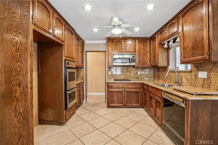 Kitchen - This well-appointed kitchen combines timeless character with functional design, featuring rich wood cabinetry, granite countertops, and a full granite backsplash that adds warmth and elegance throughout the space. Stainless steel appliances, including a built-in oven and microwave, complement the classic finishes, while ample cabinet storage and generous counter space provide everyday convenience. Tile flooring, recessed lighting, and an open pass-through to the adjacent living areas create a b...