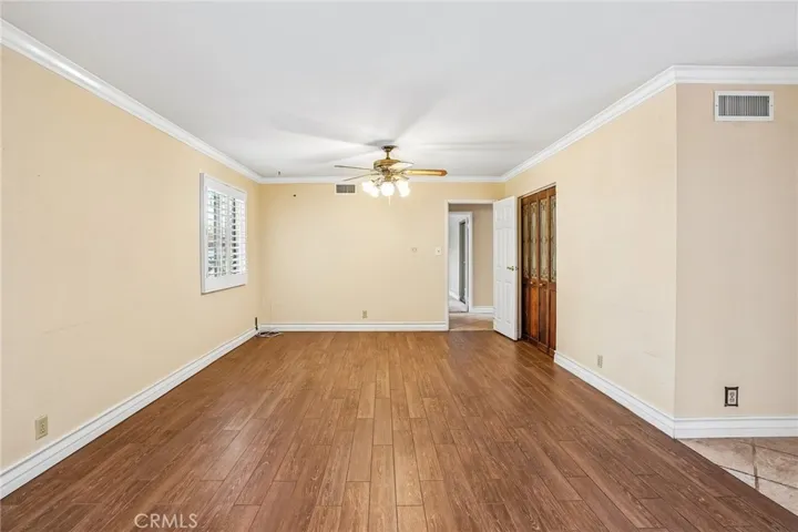 Living Room - This spacious living room offers an open and versatile layout with warm wood-style flooring, recessed lighting, and abundant natural light throughout. A cozy brick fireplace creates a welcoming focal point, complemented by a bold accent wall that adds character and charm. Plantation shutters, crown molding, and the seamless flow into adjacent living spaces make this room ideal for both relaxing and entertaining