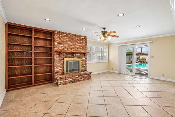 Bonus Room - This spacious bonus room offers the perfect blend of comfort and character, featuring a stunning floor-to-ceiling brick fireplace, custom built-in shelving, and an open layout ideal for entertaining or relaxing. Large windows and sliding glass doors bring in abundant natural light and provide seamless access to the backyard and pool area. With recessed lighting, tile flooring, and versatile living space, this room is ideal as a family room, game room, media space, or oversized lounge area.