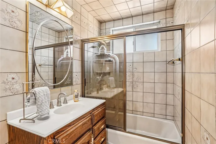 Bathroom 2 - This well-maintained bathroom features classic tile finishes with decorative floral accents that add charm and character throughout the space. The shower/tub combination is enclosed with sliding glass doors, while the updated vanity offers warm wood cabinetry paired with modern fixtures and ample storage. Natural light from the privacy window brightens the room, creating a clean and functional space with timeless appeal.