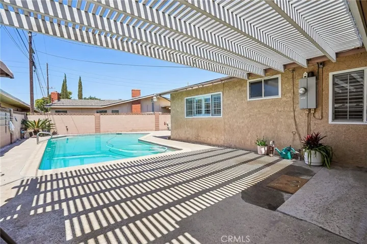 Back patio and pool - The backyard offers a private outdoor retreat centered around a sparkling pool and expansive covered patio area, perfect for relaxing or entertaining year-round. The extended pergola-style patio cover creates a unique architectural touch while providing shade and comfort for outdoor dining or lounging. With low-maintenance concrete decking, ample space for gatherings, and seamless access from the home, this backyard is designed for both functionality and enjoyment.