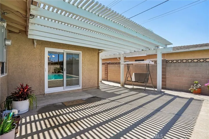 Back patio and pool - The backyard offers a private outdoor retreat centered around a sparkling pool and expansive covered patio area, perfect for relaxing or entertaining year-round. The extended pergola-style patio cover creates a unique architectural touch while providing shade and comfort for outdoor dining or lounging. With low-maintenance concrete decking, ample space for gatherings, and seamless access from the home, this backyard is designed for both functionality and enjoyment.