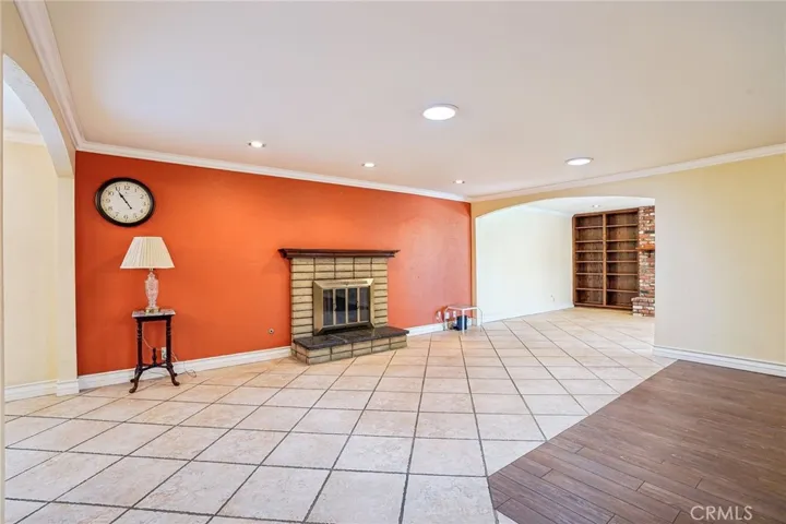 Living Room - This spacious living room offers an open and versatile layout with warm wood-style flooring, recessed lighting, and abundant natural light throughout. A cozy brick fireplace creates a welcoming focal point, complemented by a bold accent wall that adds character and charm. Plantation shutters, crown molding, and the seamless flow into adjacent living spaces make this room ideal for both relaxing and entertaining