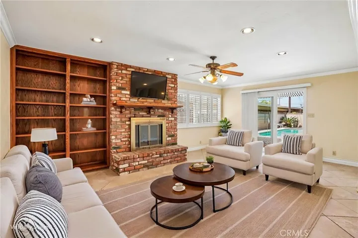Bonus Room - This spacious virtually staged bonus room offers the perfect blend of comfort and character, featuring a stunning floor-to-ceiling brick fireplace, custom built-in shelving, and an open layout ideal for entertaining or relaxing. Large windows and sliding glass doors bring in abundant natural light and provide seamless access to the backyard and pool area. With recessed lighting, tile flooring, and versatile living space, this room is ideal as a family room, game room, media space, or oversiz...