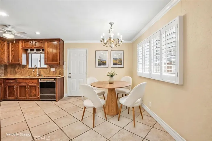 Dining Area- The inviting virtually staged dining area flows seamlessly into the kitchen, creating a warm and functional space perfect for everyday living and entertaining. The kitchen features rich wood cabinetry, ample storage, tile flooring, and a convenient breakfast bar opening to the adjacent living spaces. Natural light pours through plantation shutters, while the dining area offers an elegant chandelier and comfortable setting for gatherings with family and friends. The open layout provides both ...