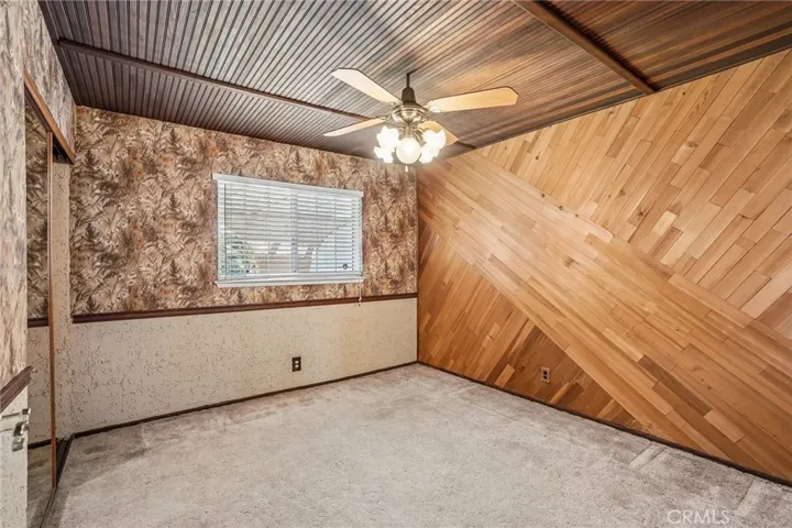 Bedroom 1 - This uniquely styled room showcases a warm rustic character with rich wood accents throughout, including a dramatic vaulted wood-plank feature wall and matching beadboard ceiling. Vintage-inspired wallpaper adds texture and personality, while the large window brings in natural light to balance the cozy ambiance. The space offers a distinctive retro charm with endless potential for customization.