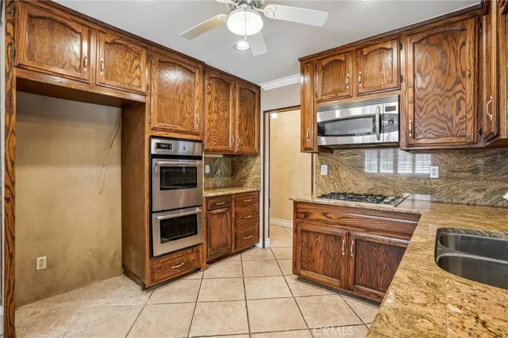 Kitchen - This well-appointed kitchen combines timeless character with functional design, featuring rich wood cabinetry, granite countertops, and a full granite backsplash that adds warmth and elegance throughout the space. Stainless steel appliances, including a built-in oven and microwave, complement the classic finishes, while ample cabinet storage and generous counter space provide everyday convenience. Tile flooring, recessed lighting, and an open pass-through to the adjacent living areas create a​​‌​​​​‌​​‌‌​​‌​​​‌‌​​​‌​​‌‌​​‌‌​​‌‌​​​​ b...