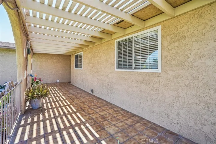 Front Porch - The covered front porch creates a warm and welcoming entrance with its distinctive arched design, tiled flooring, and extended pergola-style covering that provides both shade and character. The spacious layout offers the perfect setting for outdoor seating, morning coffee, or relaxing evenings while overlooking the beautifully maintained front lawn. Decorative wrought iron accents and natural light filtering through the overhead beams add charm and curb appeal to this inviting outdoor space.