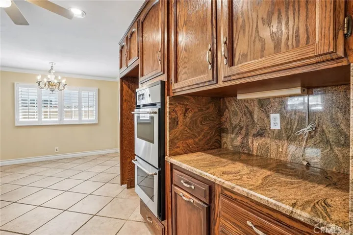 Kitchen - This well-appointed kitchen combines timeless character with functional design, featuring rich wood cabinetry, granite countertops, and a full granite backsplash that adds warmth and elegance throughout the space. Stainless steel appliances, including a built-in oven and microwave, complement the classic finishes, while ample cabinet storage and generous counter space provide everyday convenience. Tile flooring, recessed lighting, and an open pass-through to the adjacent living areas create a b...