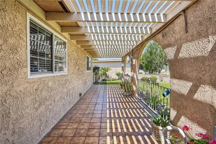 Front Porch - The covered front porch creates a warm and welcoming entrance with its distinctive arched design, tiled flooring, and extended pergola-style covering that provides both shade and character. The spacious layout offers the perfect setting for outdoor seating, morning coffee, or relaxing evenings while overlooking the beautifully maintained front lawn. Decorative wrought iron accents and natural light filtering through the overhead beams add charm and curb appeal to this inviting outdoor space.