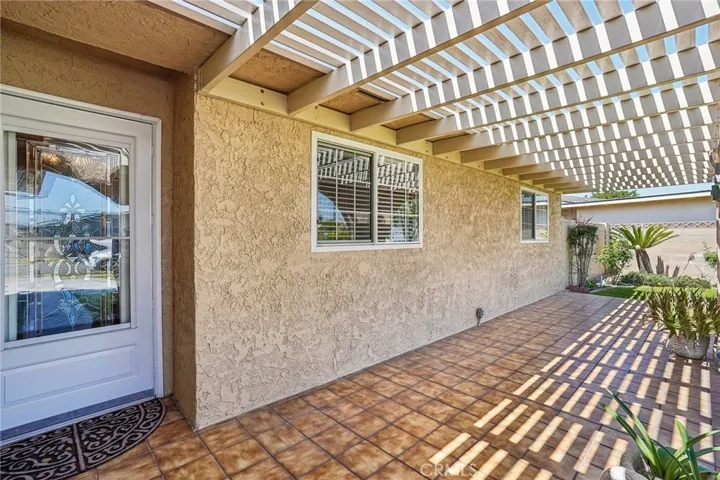 Front Porch - The covered front porch creates a warm and welcoming entrance with its distinctive arched design, tiled flooring, and extended pergola-style covering that provides both shade and character. The spacious layout offers the perfect setting for outdoor seating, morning coffee, or relaxing evenings while overlooking the beautifully maintained front lawn. Decorative wrought iron accents and natural light filtering through the overhead beams add charm and curb appeal to this inviting outdoor space.