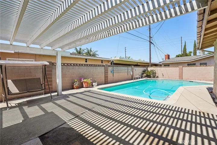 Back patio and pool - The backyard offers a private outdoor retreat centered around a sparkling pool and expansive covered patio area, perfect for relaxing or entertaining year-round. The extended pergola-style patio cover creates a unique architectural touch while providing shade and comfort for outdoor dining or lounging. With low-maintenance concrete decking, ample space for gatherings, and seamless access from the home, this backyard is designed for both functionality and enjoyment.