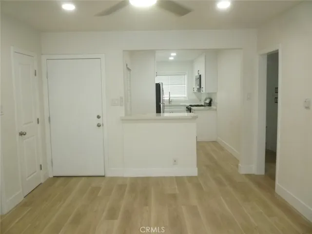 View of the front door and kitchen as seen from the living room.  Coat closet is on the left and the hallway leading to the two-bedrooms and bathroom is on the right.
