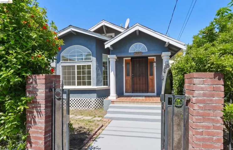 Exterior featuring a blue stucco finish, white trim, arched window accents, a decorative security screen door, and a brick gate with wrought iron detailing