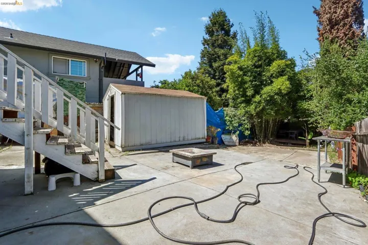 Expansive concrete patio area featuring a detached storage shed, a wood-framed stair structure, and perimeter fencing