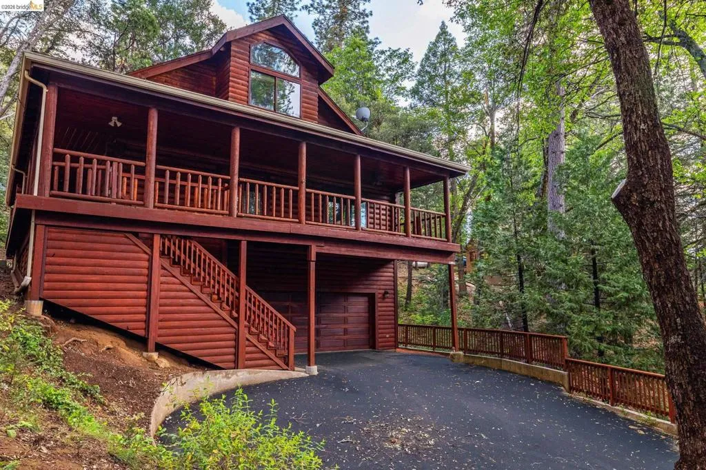 Multi-level log-sided cabin with wrap-around upper deck, wood railing, and paved driveway. Mature pines frame the full facade of this 3,171 sq ft Twain Harte retreat.