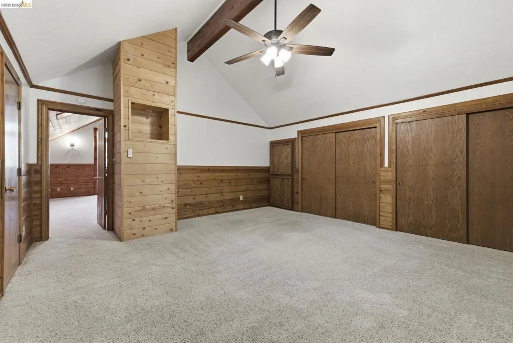 Bedroom with carpet flooring, vaulted ceiling, large multi-pane windows, and knotty pine walls. Good natural light and treetop views.