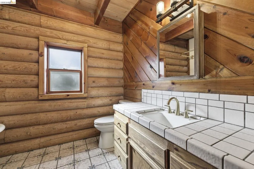 Full bathroom with log wall detail, single vanity, and tile flooring. Window provides natural light.