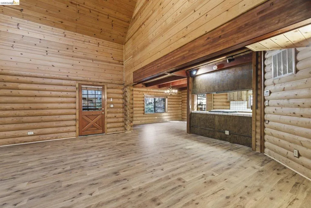 Wide-angle view of open-concept main level with knotty pine walls, wood-look flooring, and kitchen pass-through visible. Ceiling height and natural light showcase the open​​‌​​​​‌​​‌‌​​‌​​​‌‌​​​‌​​‌‌​​‌‌​​‌‌​​​​ layout.