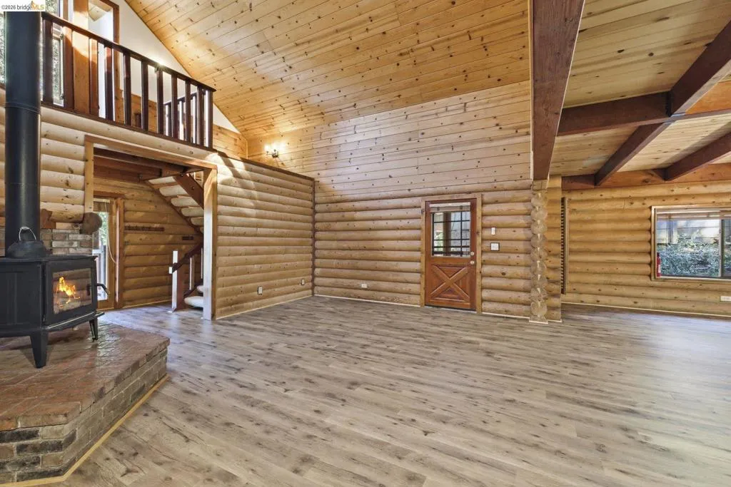 Great room showing wood-burning stove open loft above with wood railing, and open-concept connection to the main living area. Knotty pine walls throughout.