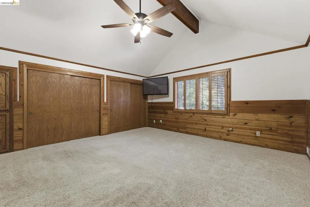 Bedroom with log wall construction, carpet flooring, ceiling fan, and window with natural light. Consistent warm wood tones throughout.
