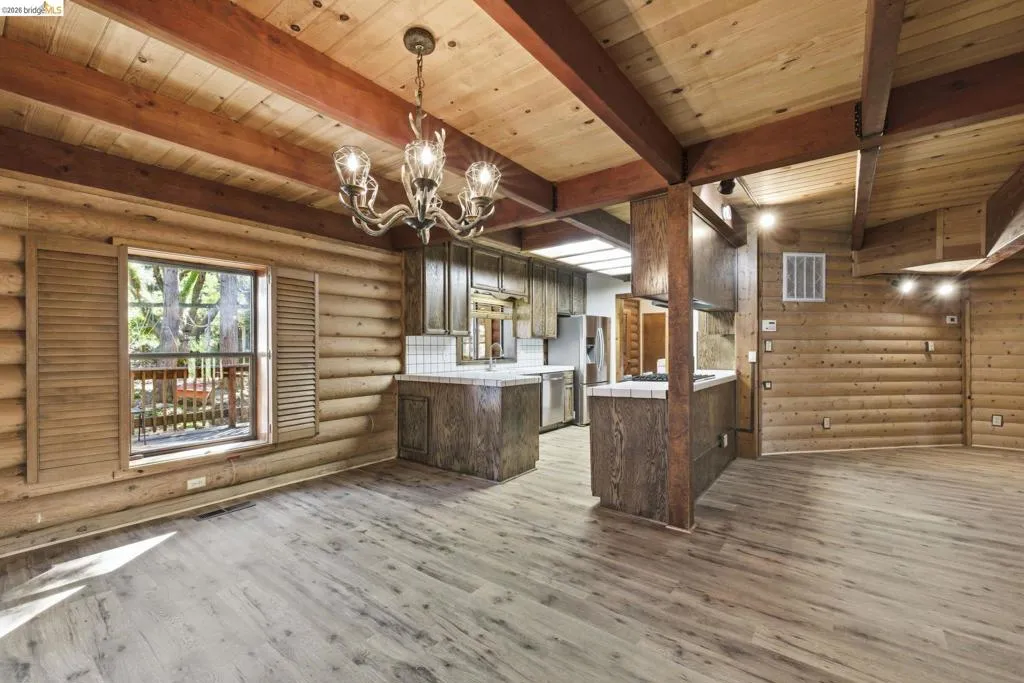 Living area showing chandelier, knotty pine walls, wood-look flooring, and connection to kitchen island. Open-concept layout with consistent warm wood finishes throughout.