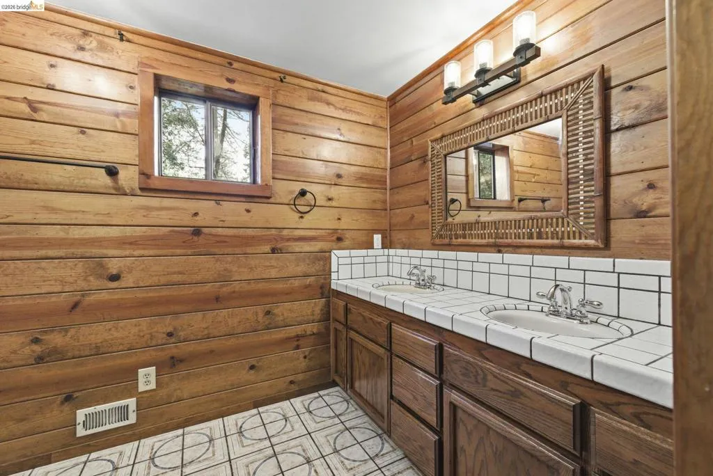 Full bathroom with double vanity, tile flooring, and knotty pine wall detail. Functional layout with adequate counter space and storage.