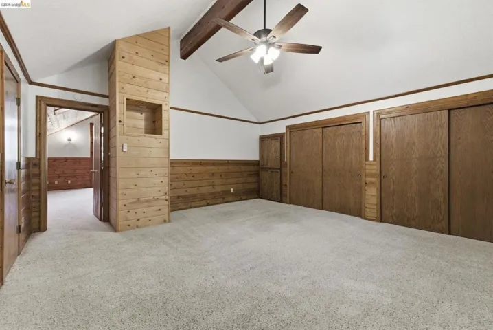 Bedroom with carpet flooring, vaulted ceiling, large multi-pane windows, and knotty pine walls. Good natural light and treetop views.