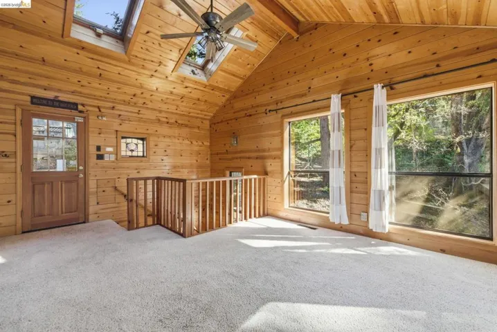 Upper-level bedroom or loft space with vaulted wood ceiling, skylight, open railing to level below, and carpet flooring. Abundant natural light from skylight above.