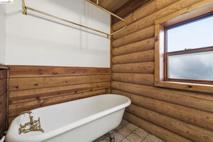 Full bathroom featuring a freestanding soaking tub, knotty pine walls, tile flooring, and window with natural light. A rare detail in a mountain cabin of this size.