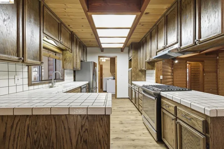 Kitchen with tile countertops, knotty pine cabinetry, center island, and wood-look flooring. Recessed lighting and open layout with pass-through to dining area.