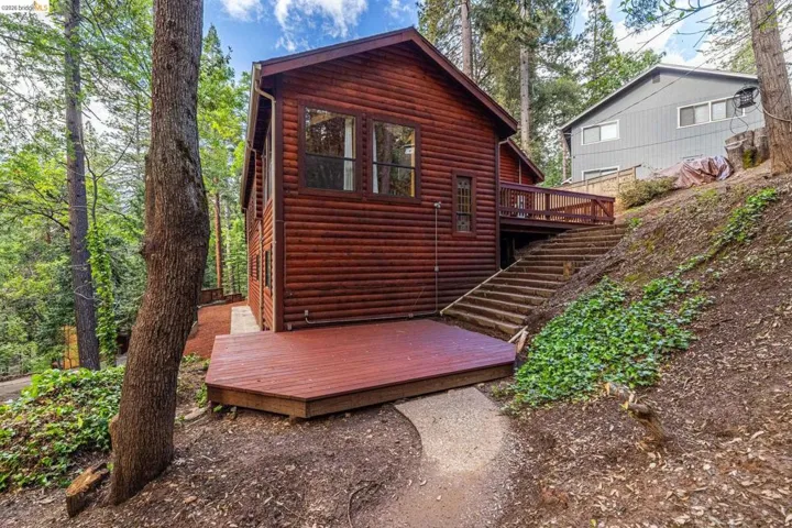 Side exterior showing garage entry and upper-level deck access. Wood siding, shingle roof, and natural grade of the 0.29-acre sloped lot.
