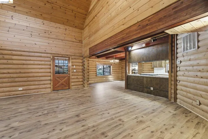 Wide-angle view of open-concept main level with knotty pine walls, wood-look flooring, and kitchen pass-through visible. Ceiling height and natural light showcase the open​​‌​​​​‌​​‌‌​​‌​​​‌‌​​​‌​​‌‌​​‌‌​​‌‌​​​​ layout.