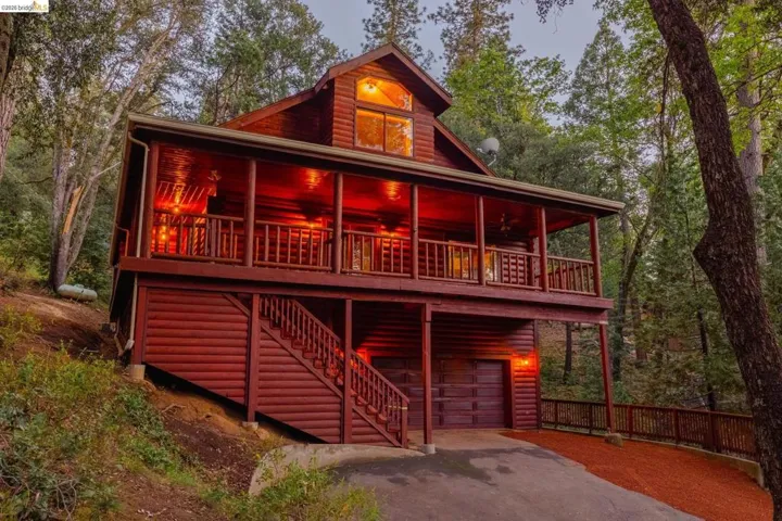 Twilight exterior shot showing the full multi-level facade lit from within. Wrap-around upper deck and lower entry deck illuminate the scale of this five-bedroom Twain Harte cabin.