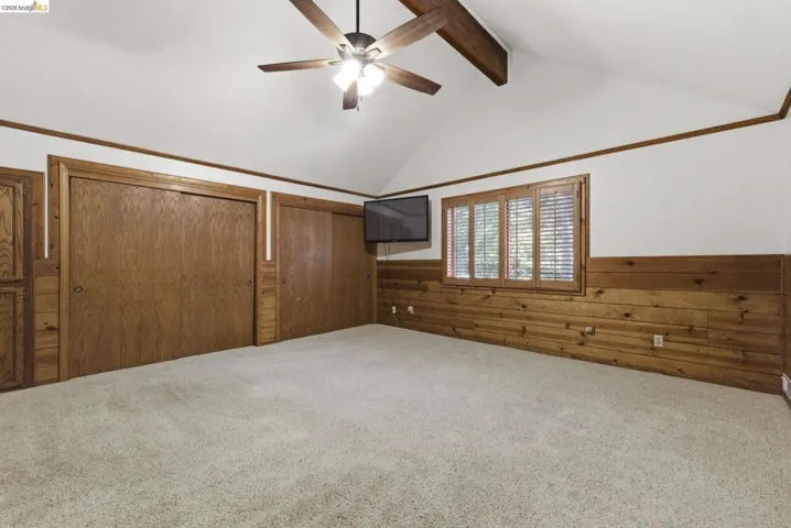 Bedroom with log wall construction, carpet flooring, ceiling fan, and window with natural light. Consistent warm wood tones throughout.