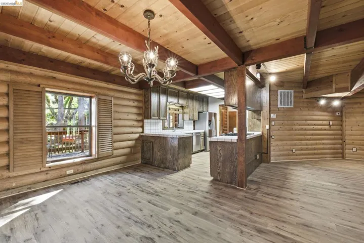Living area showing chandelier, knotty pine walls, wood-look flooring, and connection to kitchen island. Open-concept layout with consistent warm wood finishes throughout.