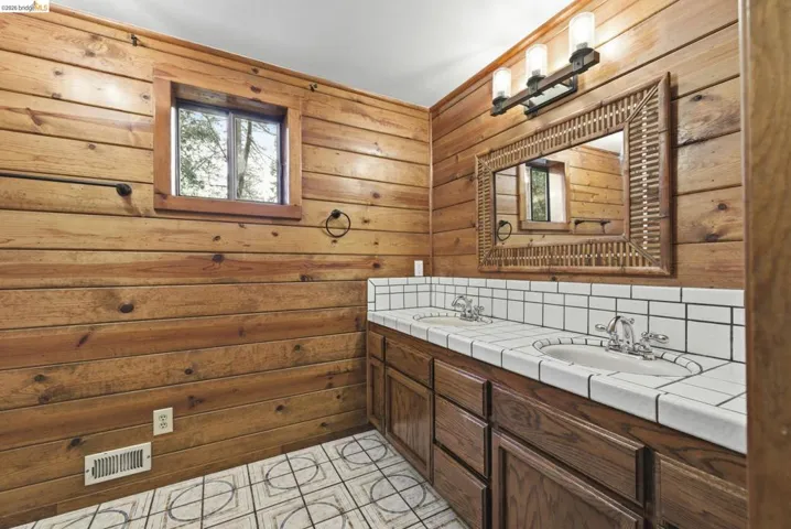 Full bathroom with double vanity, tile flooring, and knotty pine wall detail. Functional layout with adequate counter space and storage.
