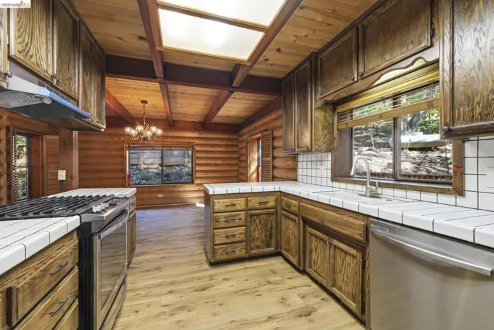 Wide-angle kitchen view showing full cabinet run, tile countertops, center island, recessed lighting, and connection to bonus room. Ample counter space and storage for a full household or rental.