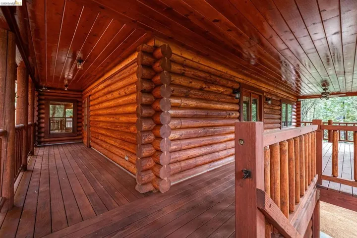 Rear exterior view showing multi-level structure, lower deck, and attached garage bay. Wooded lot with mature pines and driveway access visible.