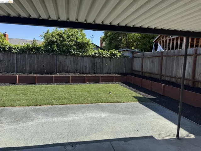 Covered patio area with a concrete surface, featuring a manicured lawn and raised wood planters
