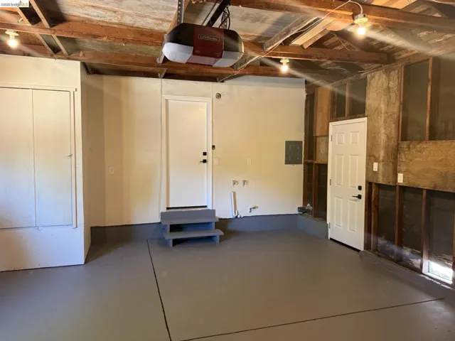 Spacious garage featuring a freshly painted concrete floor, exposed wood beam ceiling, built-in storage cabinet, and two entry doors