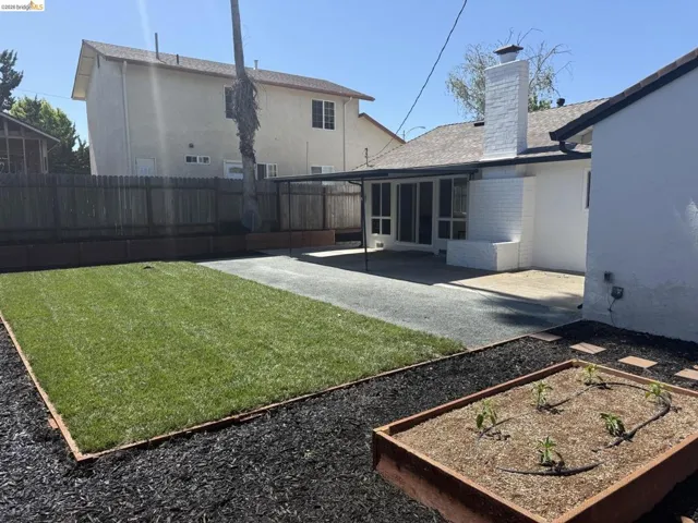 Rear exterior featuring a covered patio, exposed aggregate patio, and a white brick fireplace