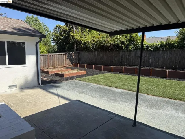 Expansive backyard featuring a covered patio, concrete paving, a manicured lawn area, and raised garden beds