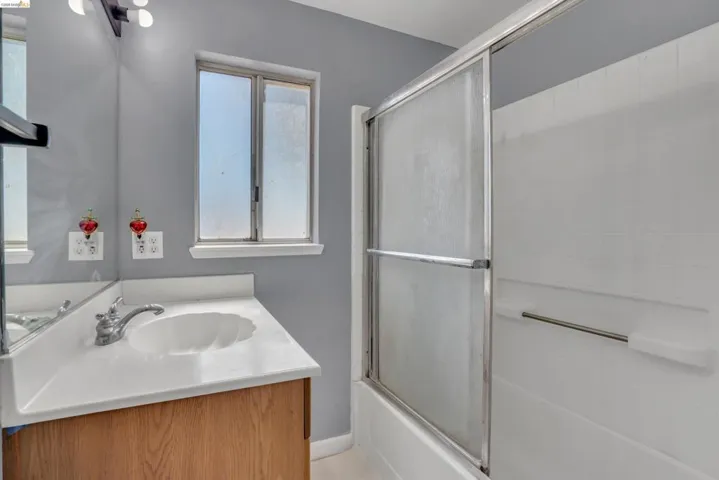 Full bathroom featuring a single vanity with wood-finish cabinetry, a white countertop with an integrated sink, and a shower-tub combination with sliding glass doors