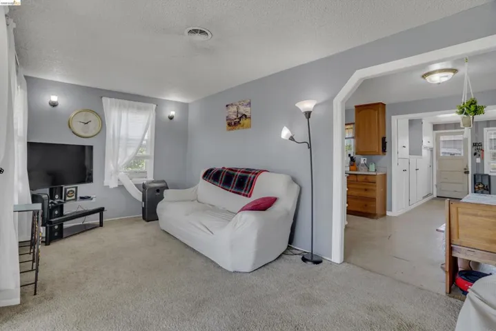 Living area featuring light gray wall paint, textured ceiling, a window with blinds, and wall-mounted light fixtures