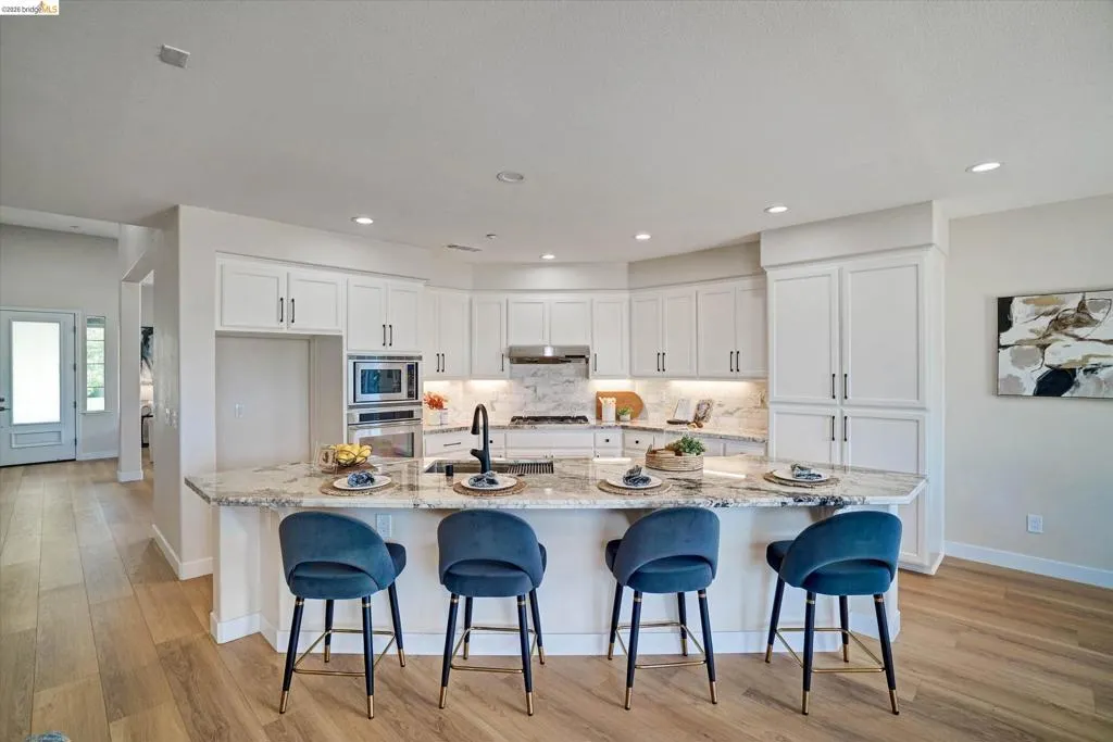 Modern kitchen featuring a large central island with seating, light-toned cabinetry, stainless steel appliances, and wood-finish flooring