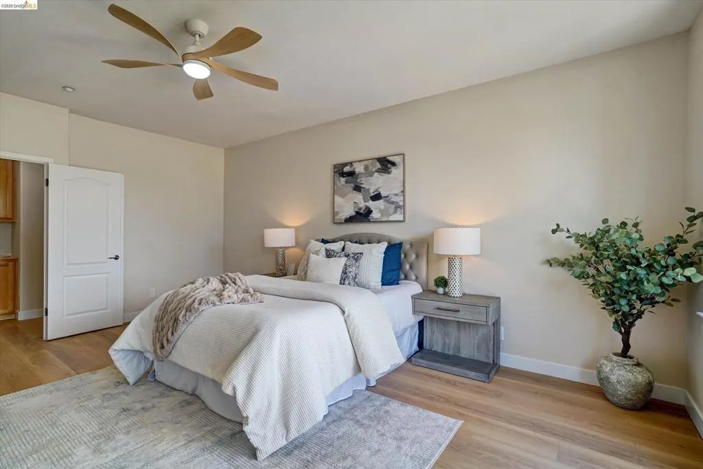 Bedroom featuring wood-finish flooring, a contemporary ceiling fan with integrated lighting, and a white paneled door