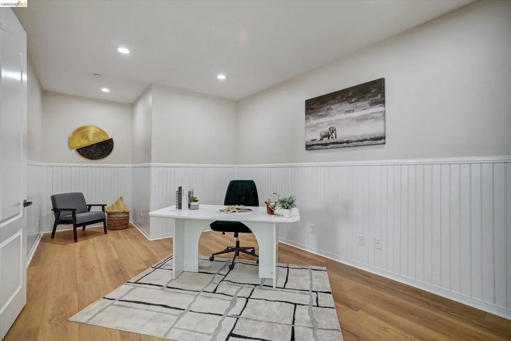 Room featuring wood-finish flooring, white beadboard wainscoting, recessed lighting, and a paneled door. Could be 5th bedroom.