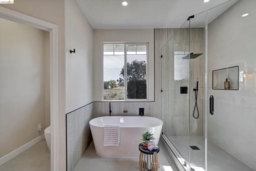 Contemporary bathroom featuring a freestanding soaking tub with wall-mounted faucet, a spacious glass-enclosed shower with rain head, large format tile flooring, and integrated shower niche